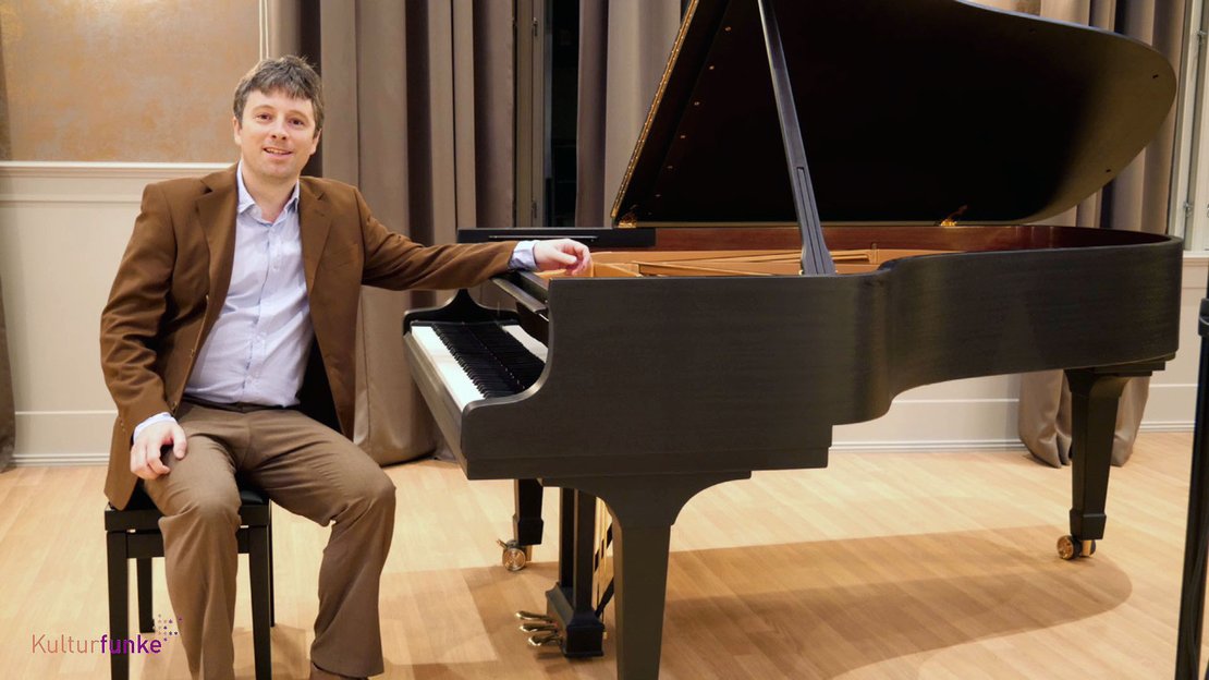 Der Pianist Daniel Fritzen sitzt an einem schwarzen Konzertflügel und lächelt in die Kamera.